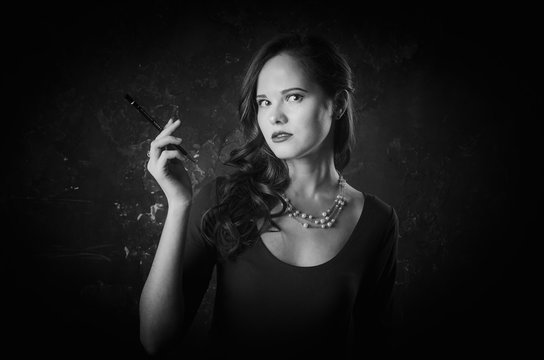 Noir film style woman in dress holding cigarette standing back to camera. Female posing with gun. Black and white photography. Old fashion photo