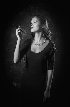 Noir film style woman in dress holding cigarette standing back to camera. Female posing with gun. Black and white photography. Old fashion photo