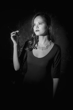 Noir film style woman in dress holding cigarette. Black and white photography. Old fashion photo