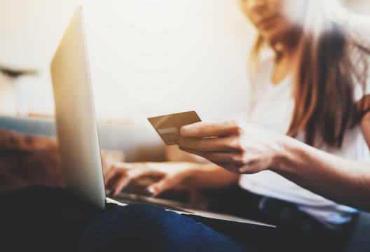 Closeup of female hands holding credit card to pay online via modern laptop, hipster girl with long hair using debit card paying for shopping online in internet, flare light