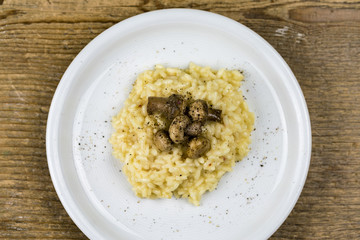 Still Life of Creamy Risotto Rice with Sauteed Mushrooms Seasoned with Black Pepper and Served on White Plate on Rustic Wooden Table