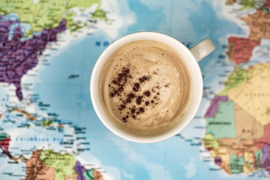 Cup of coffee with cinnamon from above over world map background surface