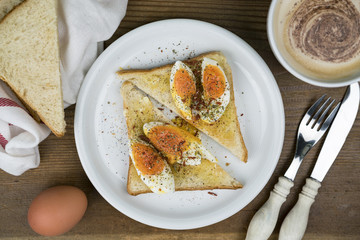 Hard boiled egg sandwich seasoned with pepper served with a mug of frothy cappuccino with utensils and ingredients