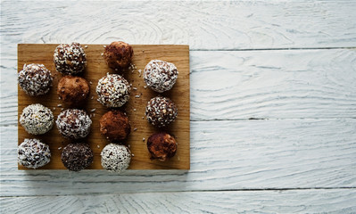 Healthy raw energy balls with cocoa, coconut, sesame, chia on a white textured wooden background.  Vegan chocolate truffles. Copy space