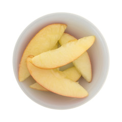 Red apple slices in a small white bowl top view.