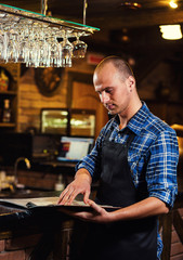 Barman at work in pub,Portrait of cheerful barman worker standing,Waiter giving menus,A pub.Bar.Restaurant.Classic.Evening.European restaurant.European bar.American restaurant.American bar.
