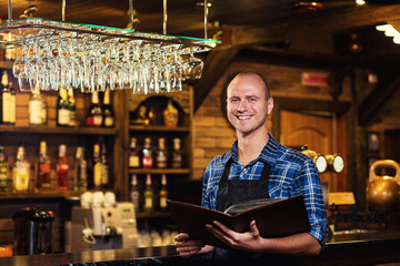 Barman at work in pub,Portrait of cheerful barman worker standing,Waiter giving menus,A pub.Bar.Restaurant.Classic.Evening.European restaurant.European bar.American restaurant.American bar.