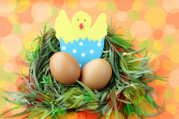 easter decoration: yellow eggs and hand made hatched chicken in eggshell in green grass twigs nest on bright colorful  background with copy space