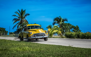 Amerikanischer gelber Oldtimer fährt auf der Küstenstraße nach Santa Clara Kuba - Serie Kuba Reportage