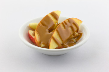 Apple slices covered with peanut butter in a small bowl atop a white tablecloth.