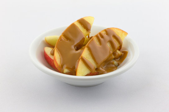 Apple Slices Covered With Peanut Butter In A Small Bowl Atop A White Tablecloth.