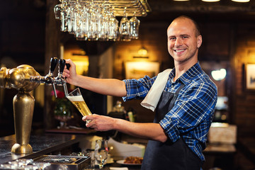 Bartender pouring the fresh beer in pub,barman hand at beer tap pouring a draught lager beer,beer from the tap,Filling glass with beer,fresh beer,pub.Bar.Restaurant.European bar.American bar.