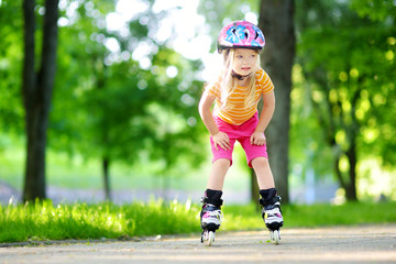 Pretty little girl learning to roller skate on beautiful summer day in a park