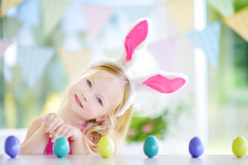 Cute little girl wearing bunny ears playing egg hunt on Easter