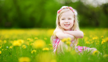 Adorable little girl in blooming dandelion meadow on beautiful spring day