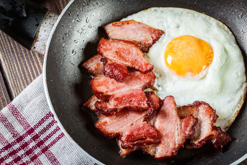 Slices of smoked bacon and fried egg in frying pan
