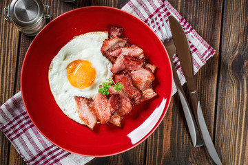 Slices of smoked bacon and fried egg on a red plate