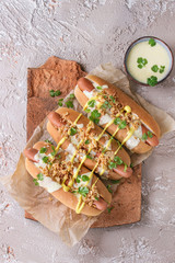 Hot dogs with sausage, fried onion, coriander leaves, cheese sauce and mustard, served on terracotta board over beige concrete texture background. Fast food. Top view, copy space