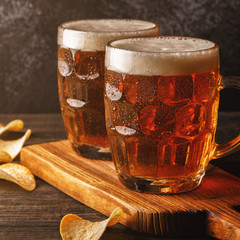 Cold beer in glass with chips on a dark background.