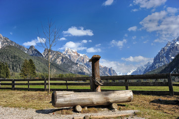 Landscape of Dolomites mountains in summer with a fountain near a fence