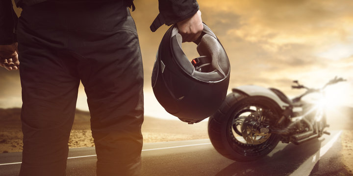 Motorradfahrer steht mit Motorrad auf einer Stra&szlig;e 