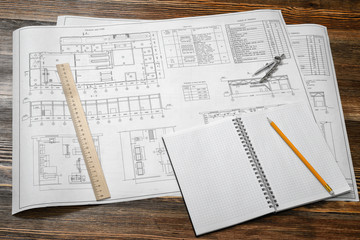 Open blueprints on wooden table background with a pencil, a ruler and compasses lying beside.