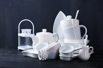 Set of new white dishes with teapot, tea cups, and plates on a black wooden table