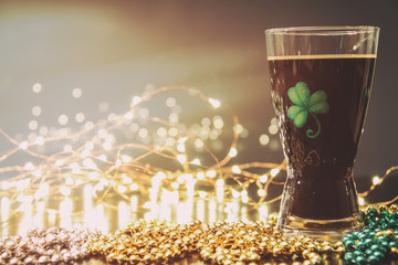 St Patricks Day Irish Stout Beer. Traditional Irish stout, a dark beer. On a pub bar rail table with lights and St Patrick's Day party beads.