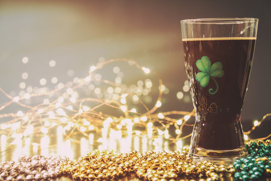 St Patricks Day Irish Stout Beer. Traditional Irish Stout, A Dark Beer. On A Pub Bar Rail Table With Lights And St Patrick's Day Party Beads.