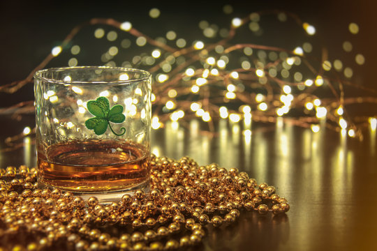 Irish Whiskey St Patricks Clover. Irish whiskey in a glass with a clover symbol, on a pub table with gold beads and bar lights.