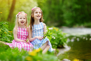 Two adorable little sisters playing by a river in sunny park on a beautiful summer day