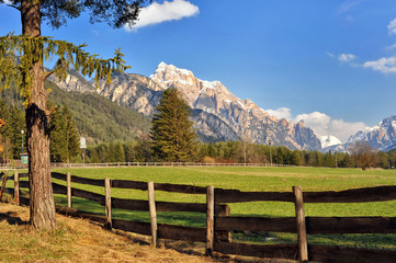 Fototapeta na wymiar Landscape of Dolomites mountains in summer with a farm and meadows near a fence