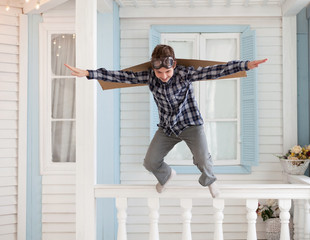 Happy boy jump with cardboard boxes of wings in home dream of flying