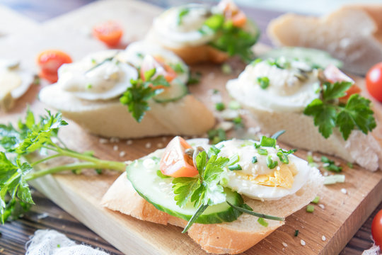 Bread with slices of fresh cucumber, egg, tomato and cream cheese on a wooden cutting board. Fresh parsley and rosemary.