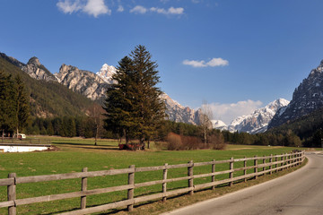 Landscape of Dolomites mountains in summer with a farm and meadows near a fence