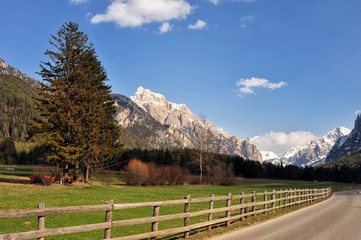 Landscape of Dolomites mountains in summer with a farm and meadows near a fence