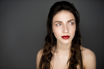 Fototapeta premium Portrait of a beautiful naked brunette girl with red lips and braids. Studio shot. Place for texte