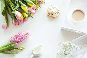 Fototapeta na wymiar Morning breakfast in spring with a cup of black coffee with milk and pastries in the pastel colors, a bouquet of fresh yellow and pink tulips on a white background. Top view.