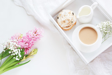 Obraz na płótnie Canvas Morning breakfast in spring with a cup of black coffee with milk and pastries in the pastel colors, a bouquet of fresh pink hyacinth on a white background. Top view.
