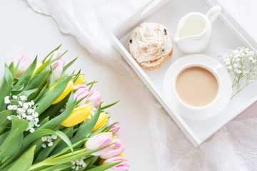 Morning breakfast in spring with a cup of black coffee with milk and pastries in the pastel colors, a bouquet of fresh yellow and pink tulips on a white background. Top view.