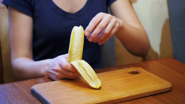 Woman Cleaning a Banana While Sitting at a Table in a Home Kitchen