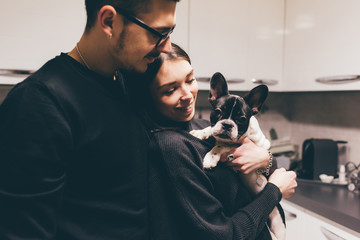 Young beautiful couple indoor in their aparment holding french bulldog puppy - family, animal,...