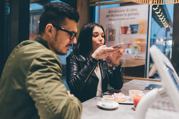 Young beautiful couple having coffee in the night using smart phone - technology, social network, communication concept