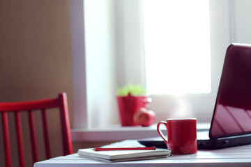 work break in red tones/ hot mug with a computer and a paper notebook at home