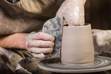 Creating mug from clay on a twisted potter's wheel. Dirty hands in the clay and the potter's wheel with the workpiece. The sculptor in the workshop makes a jug out of earthenware closeup.