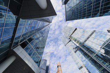 Fototapeta premium Modern business office skyscrapers, looking up at high-rise buildings in commercial district, architecture raising to the blue sky with white clouds, bottom view