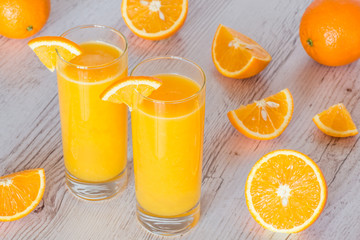 orange juice in glasses at light wooden background