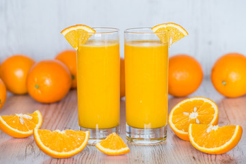 orange juice in glasses at light wooden background