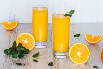 Fototapeta na wymiar orange juice with mint in glasses at light wooden background