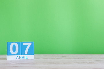April 7th. Day 7 of month, calendar on wooden table and green background. Spring time, empty space for text